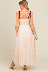 woman wearing a cream maternity maxi dress with adjustable black tie straps and a smocked back