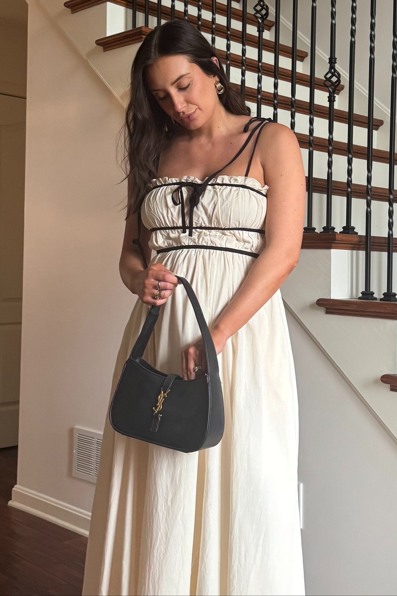 woman wearing a cream maternity maxi dress with black accents, holding a black purse and standing on a staircase