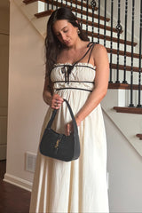 woman wearing a cream maternity maxi dress with black accents, holding a black purse and standing on a staircase