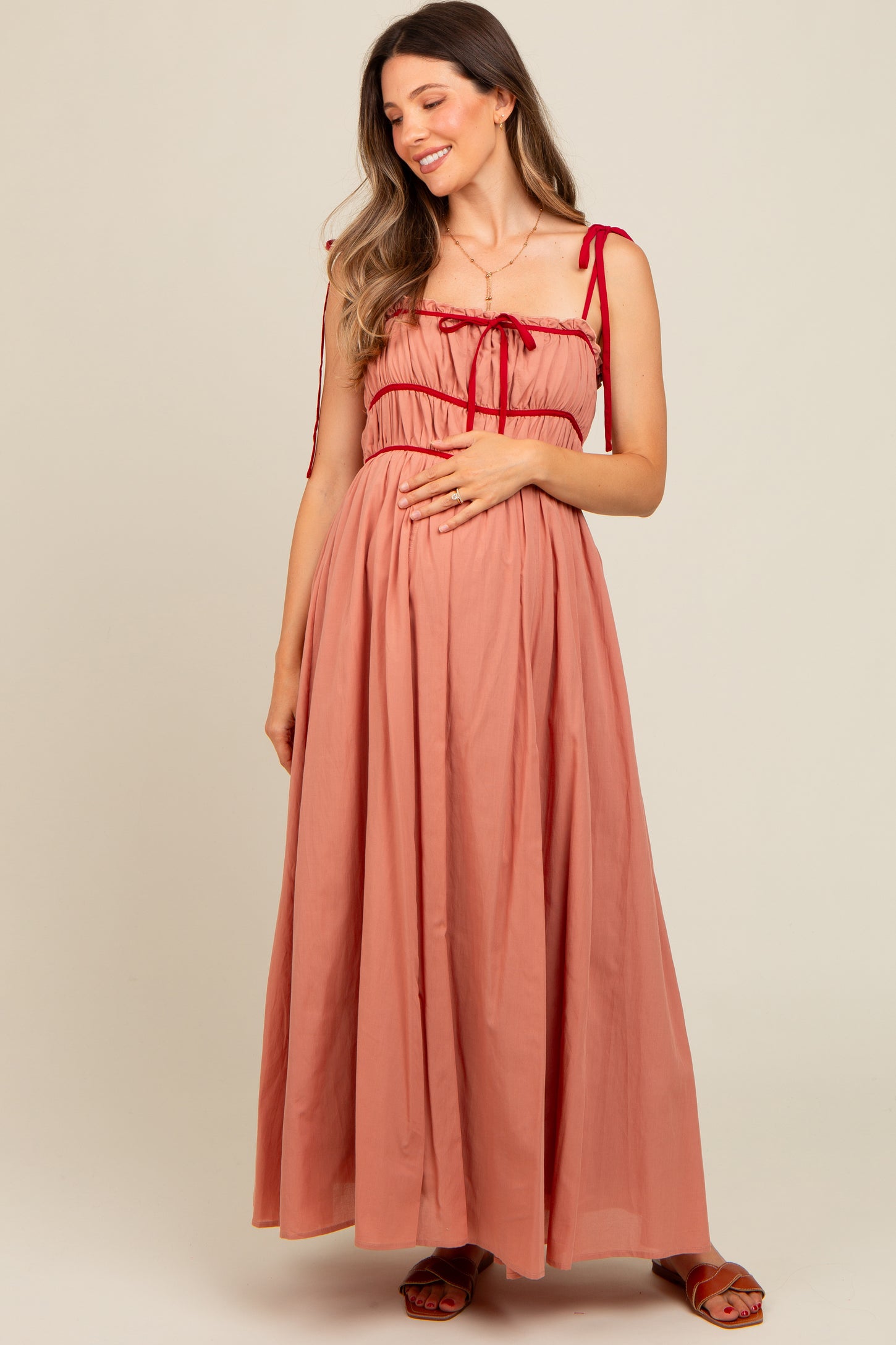 woman wearing a rose-colored maternity maxi dress with adjustable straps and a cinched bodice, holding her baby bump