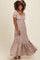 woman wearing a floral maxi dress with short puff sleeves and a tiered hem, smiling and standing against a neutral background