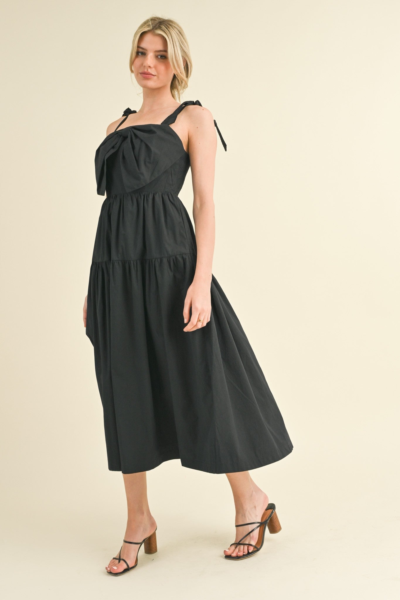 woman wearing a black maxi dress with tie straps and a tiered skirt, paired with strappy heels