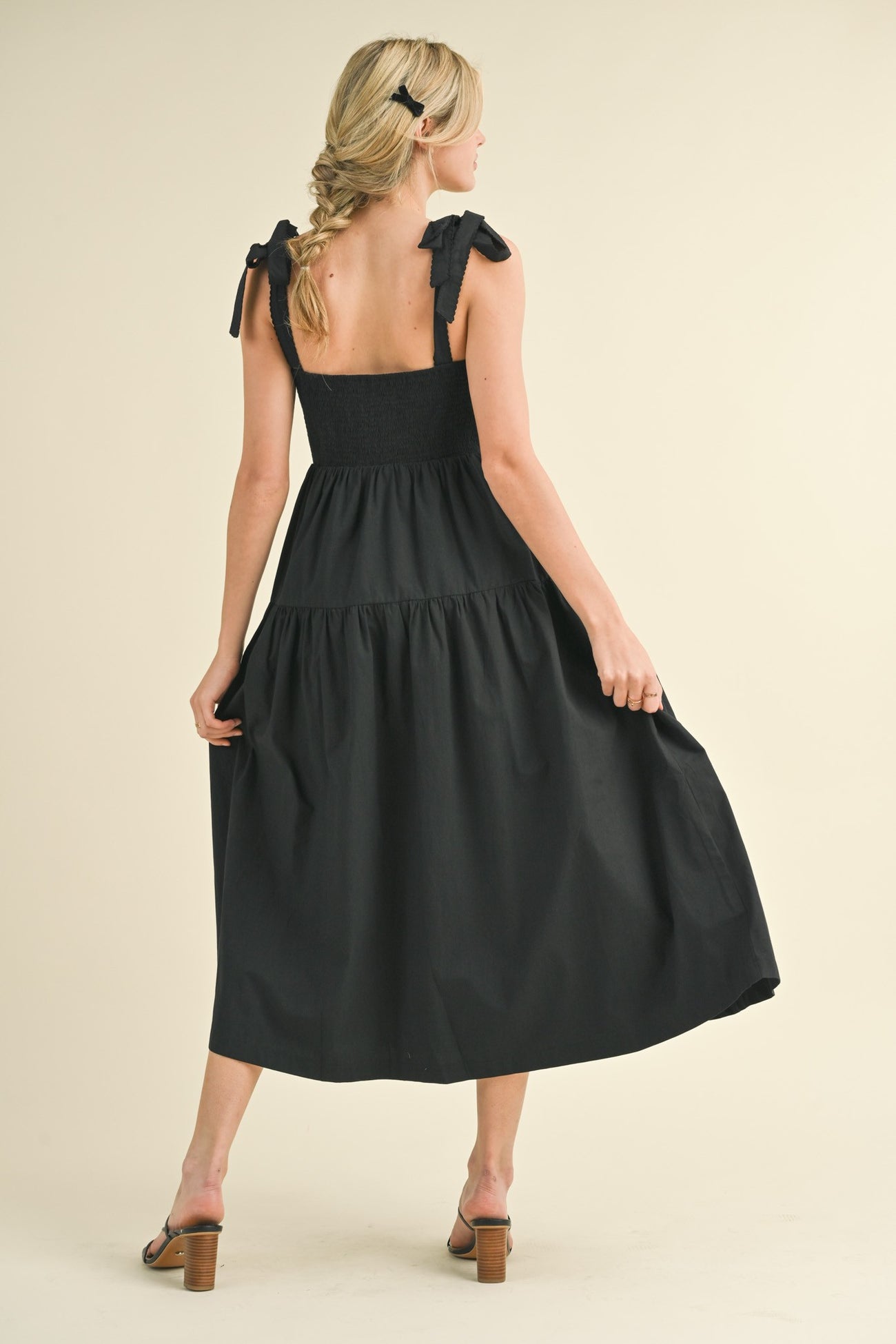 woman wearing a black maxi dress with tie straps and a smocked bodice, showing a flowy skirt and bare back