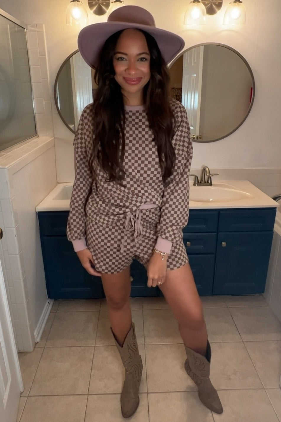 woman wearing a brown and cream checkered two-piece outfit with a tied waist, brown cowboy boots, and a wide-brim hat