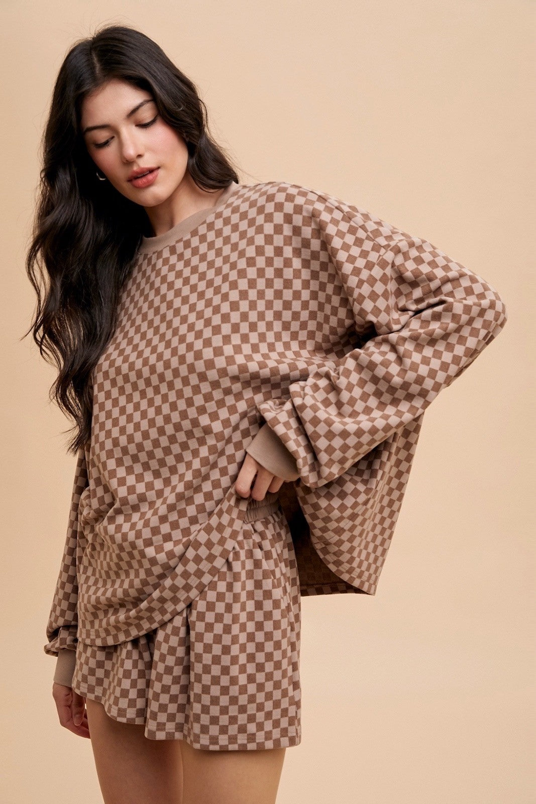 woman wearing a brown checkered oversized sweatshirt and matching skirt with a playful ruffle hem