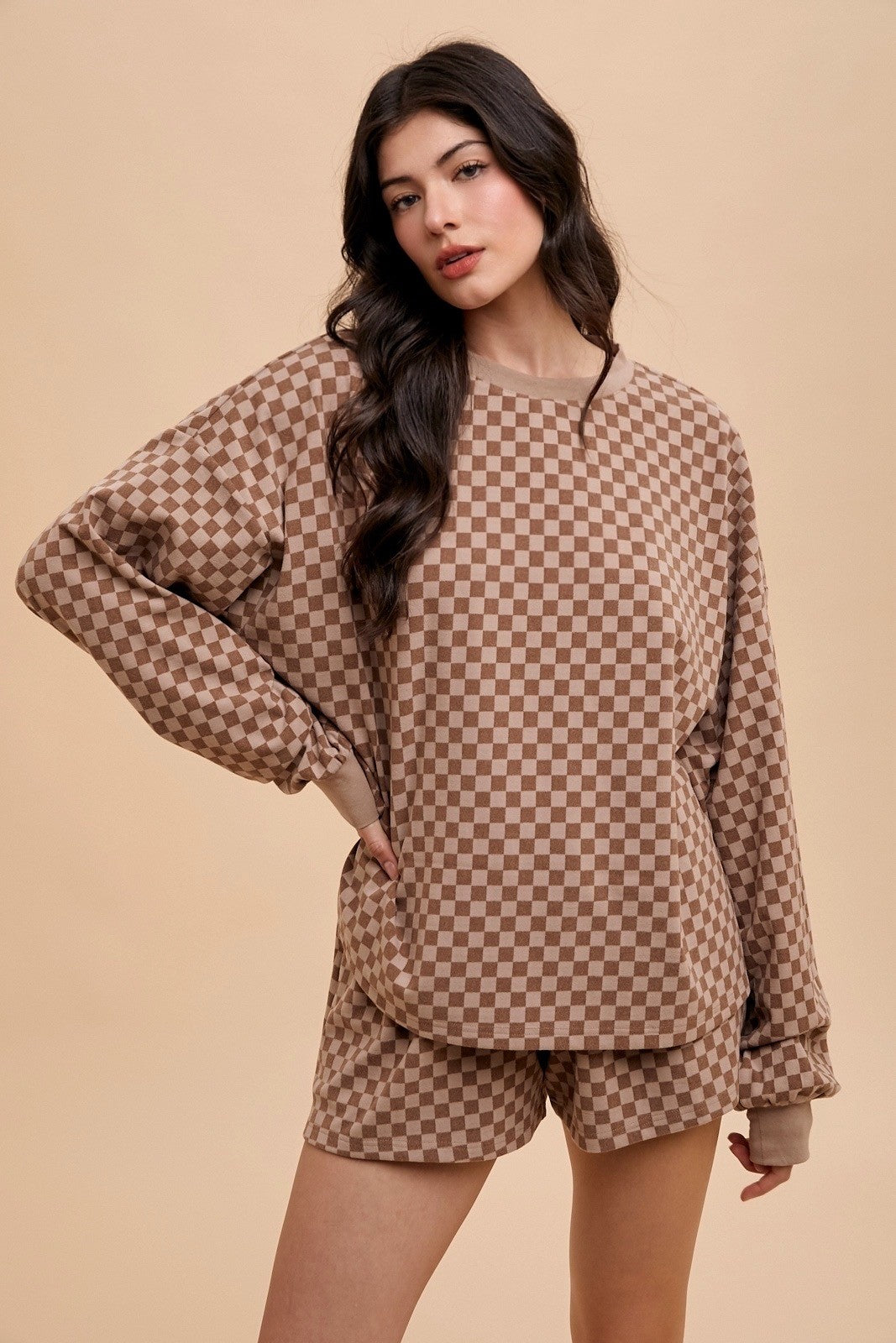 woman wearing a brown checkered long sleeve top and matching shorts, standing confidently