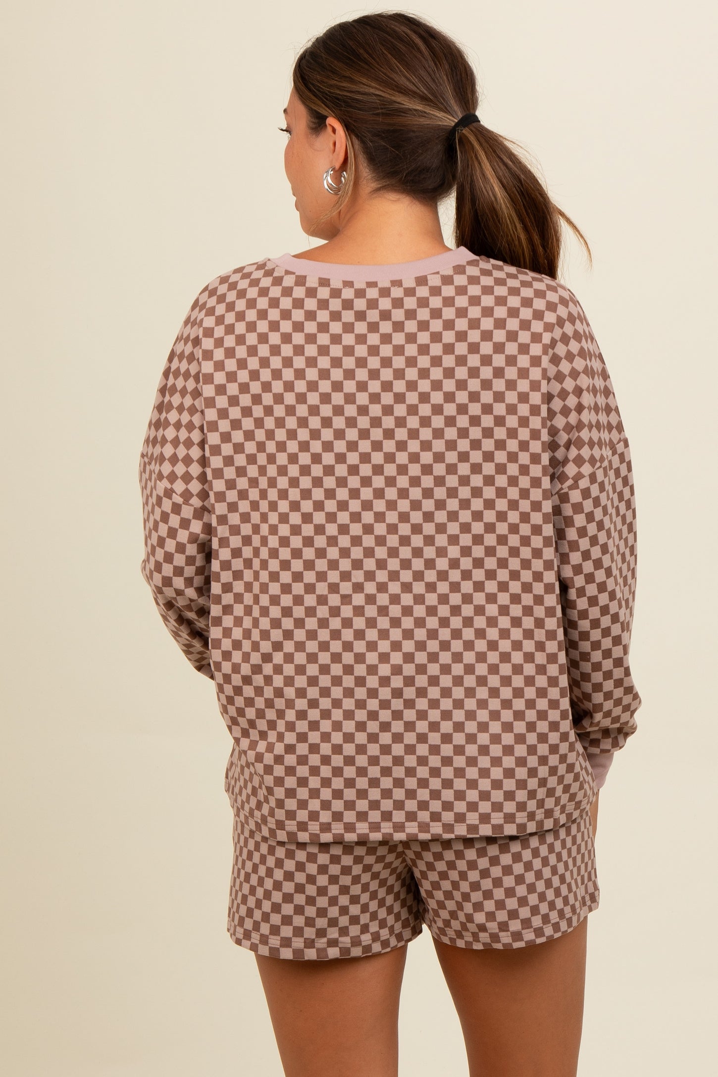 woman wearing a brown and beige checkered maternity loungewear set with long sleeves and matching shorts, seen from the back