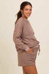 woman wearing a brown checkered maternity loungewear set with a relaxed fit top and drawstring shorts, showing her baby bump