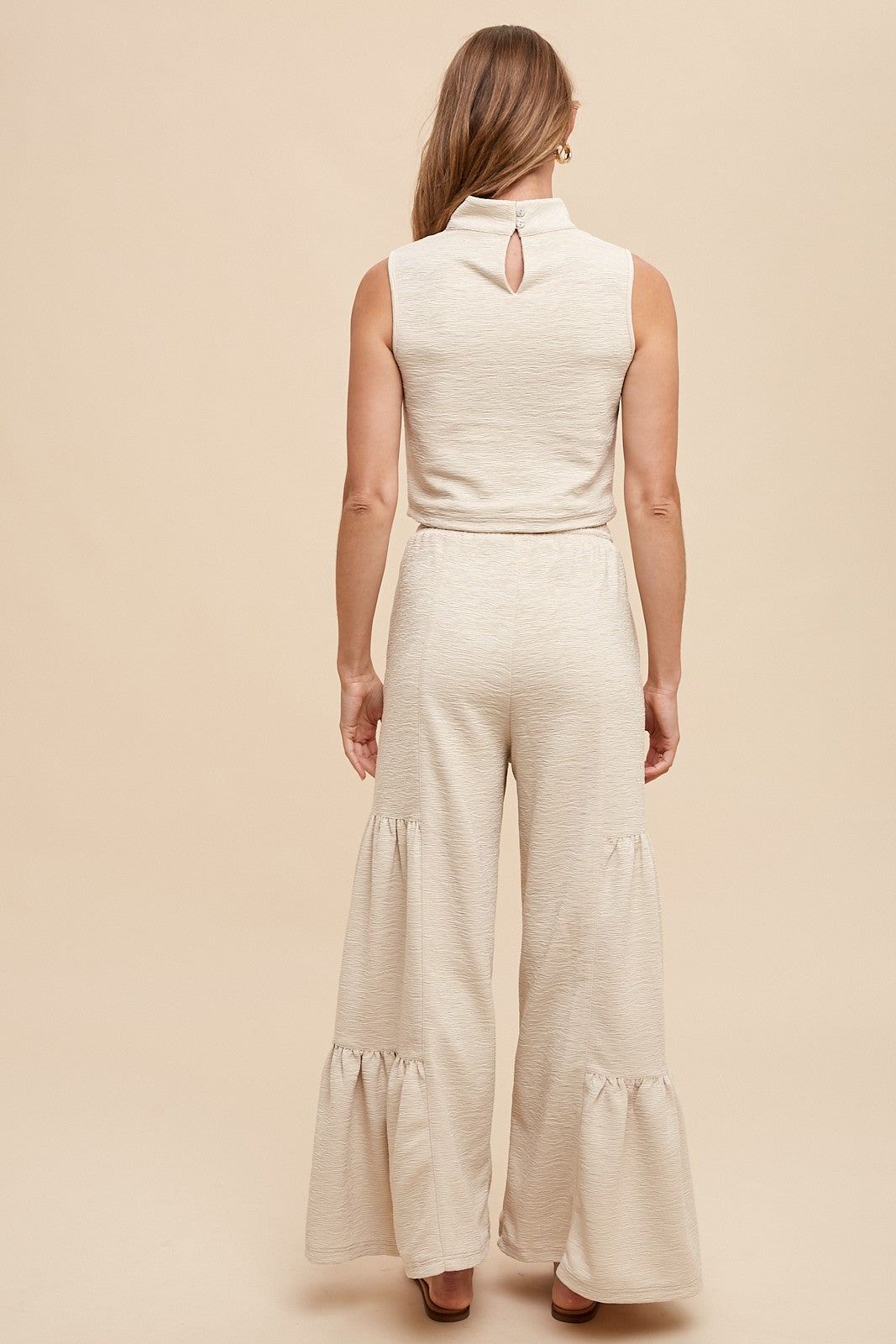 woman wearing a beige sleeveless jumpsuit with a keyhole back and ruffled wide legs