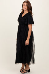 woman wearing a black maxi dress with ruffled sleeves and sheer overlay, standing in a neutral background