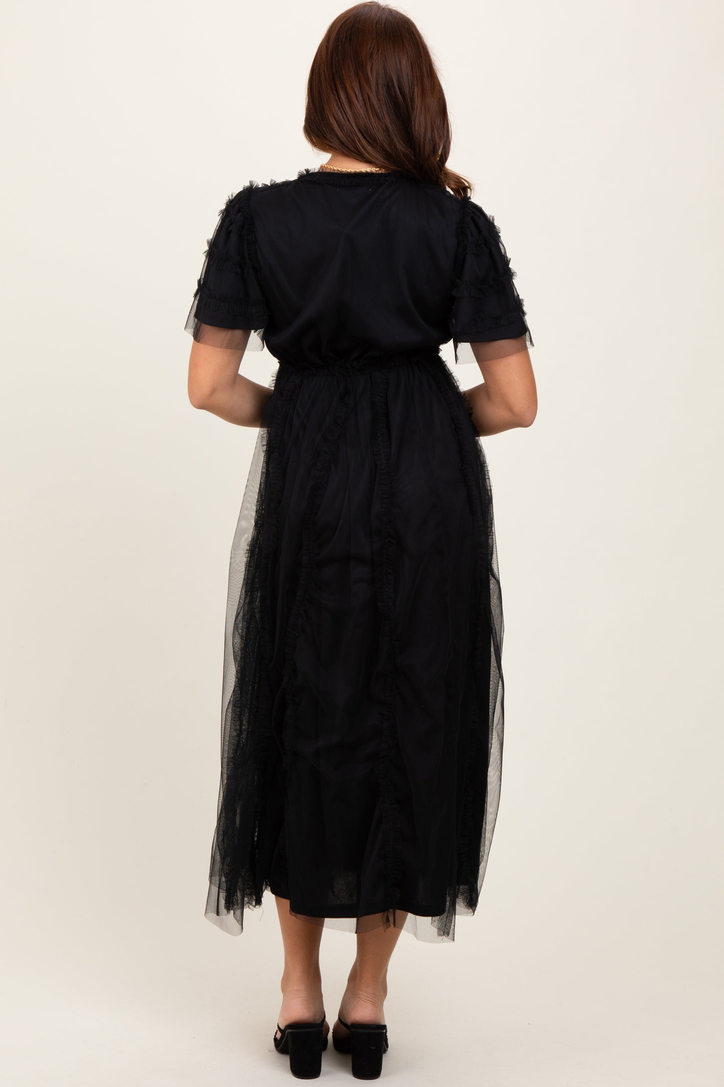 woman wearing a black maxi dress with ruffle details and a sheer overlay, shown from the back