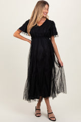 woman wearing a black maternity dress with tulle overlay and short sleeves, showcasing her baby bump