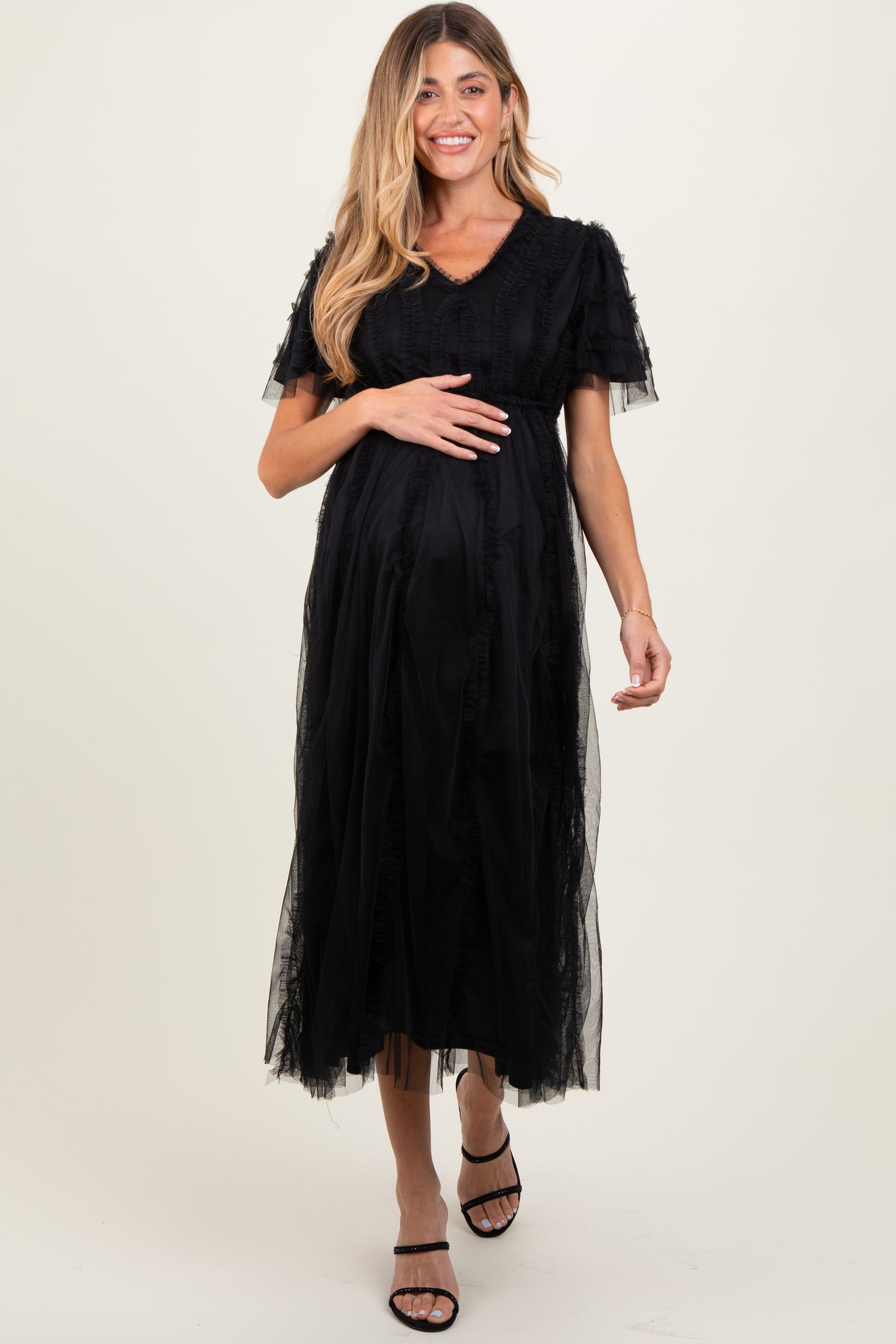 woman wearing a black maternity dress with ruffle details and short sleeves, holding her baby bump