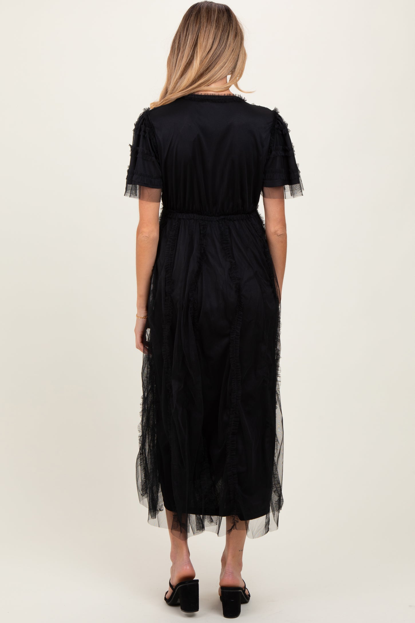 woman wearing a black maternity dress with sheer tulle details and a flowy silhouette from the back