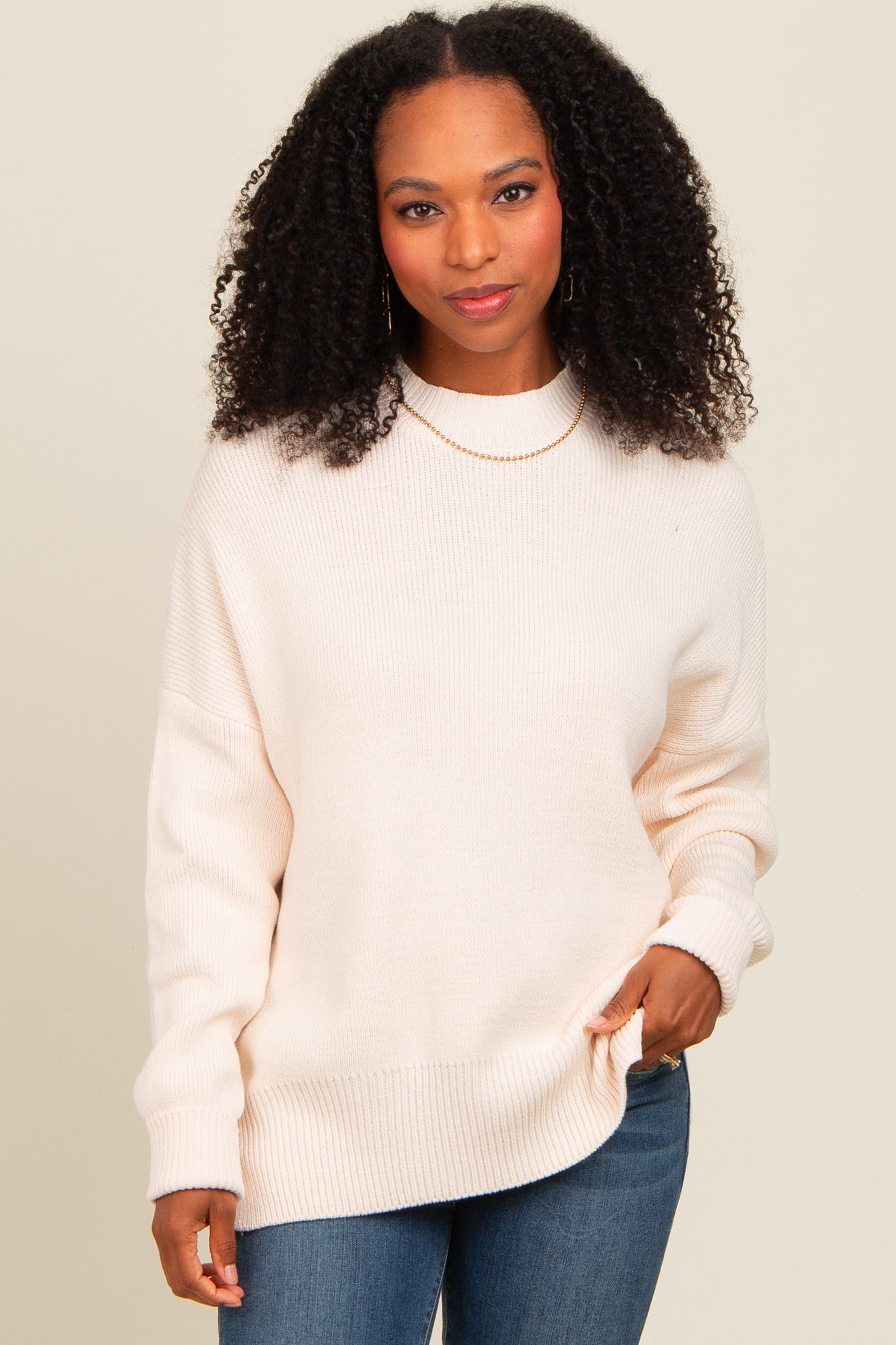 woman wearing a soft beige oversized knit sweater with long sleeves and a round neckline, styled with blue jeans