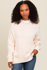 woman wearing a soft beige oversized knit sweater with long sleeves and a round neckline, styled with blue jeans