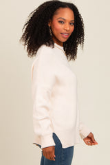 woman wearing a light pink oversized sweater with ribbed details and side slits, paired with blue jeans