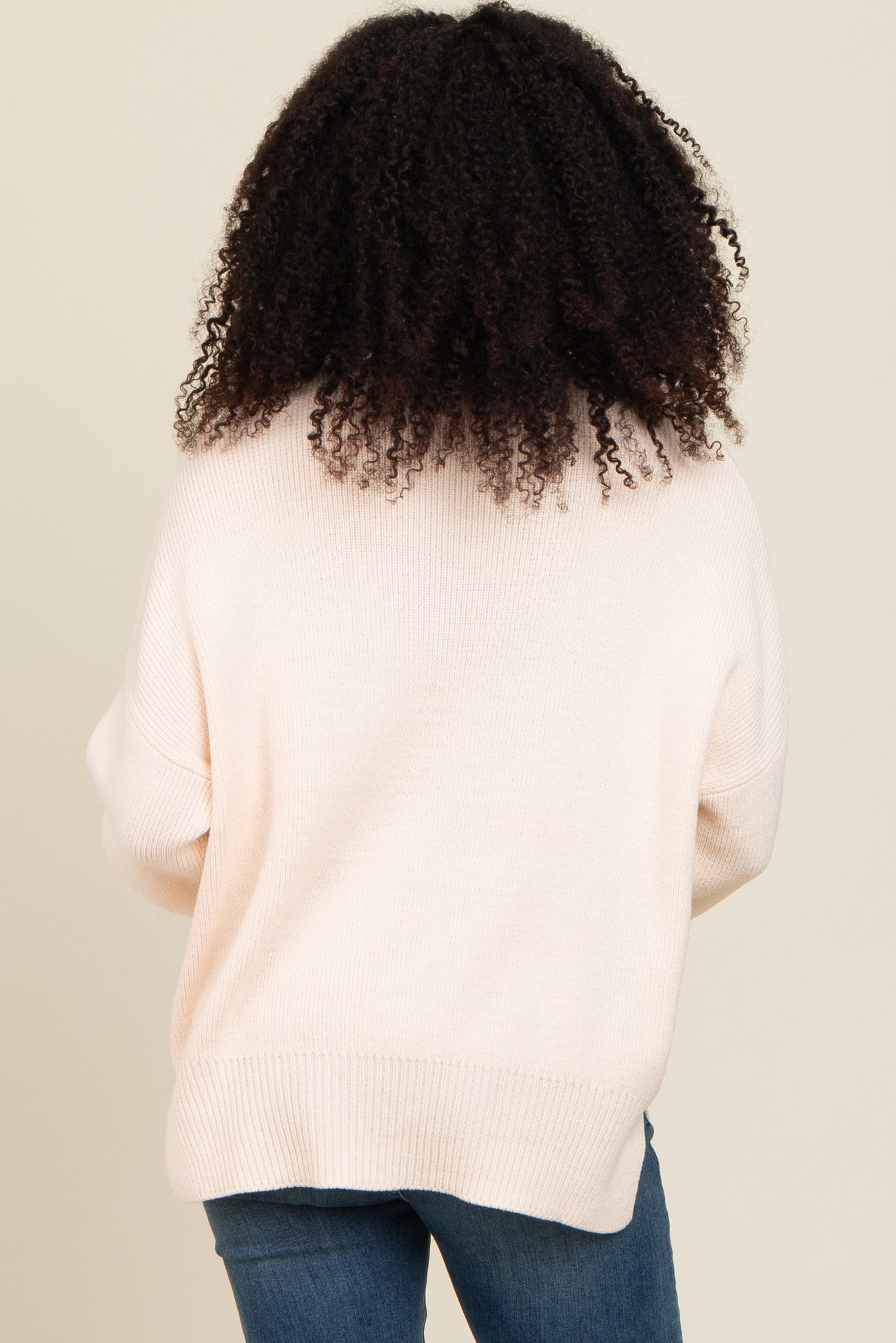 woman wearing a light pink oversized sweater from the back with a relaxed fit and ribbed hem