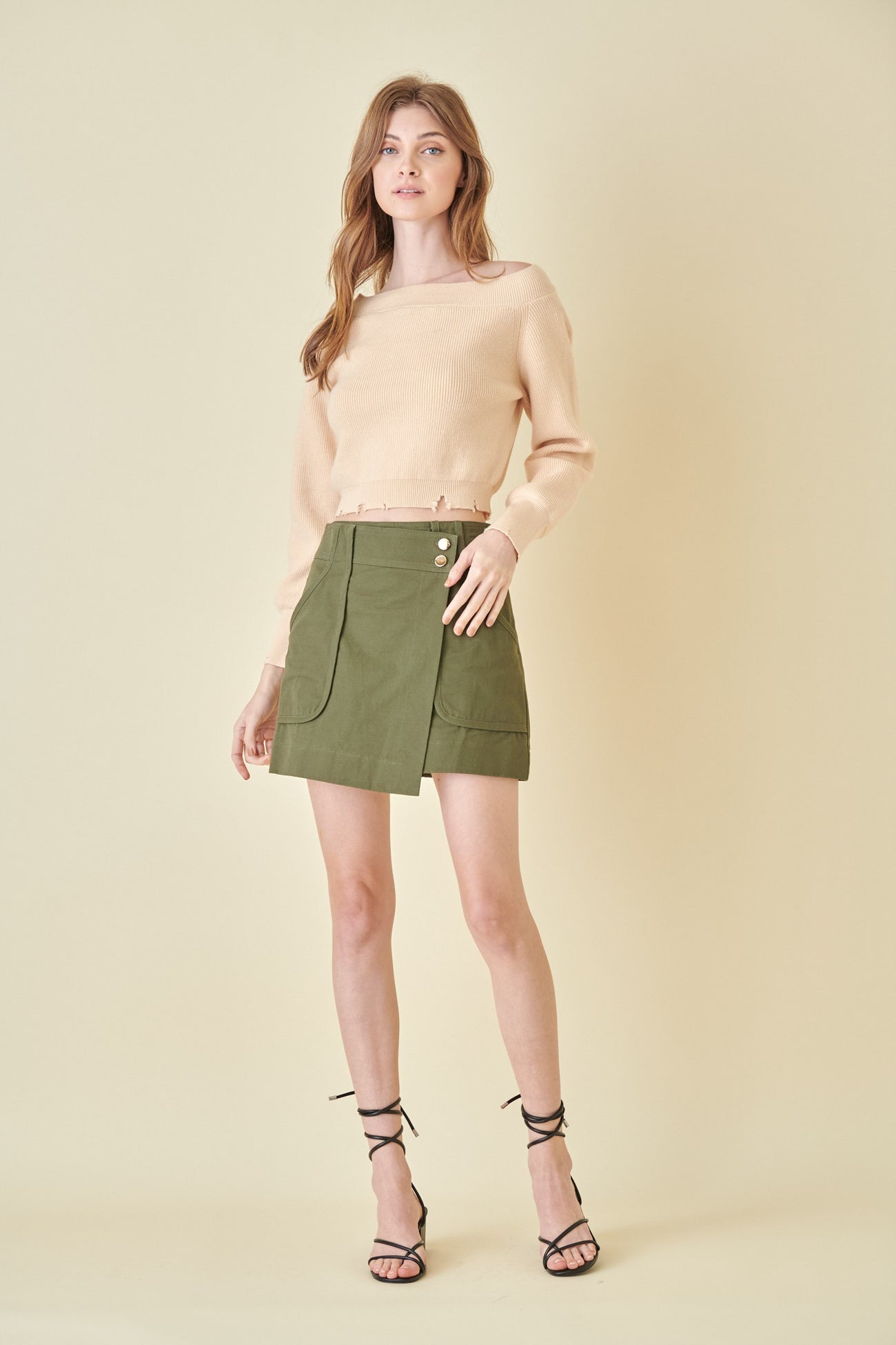 woman wearing a beige cropped sweater and an olive green mini skirt with front pockets and button details