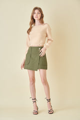 woman wearing a beige cropped sweater and an olive green mini skirt with front pockets and button details