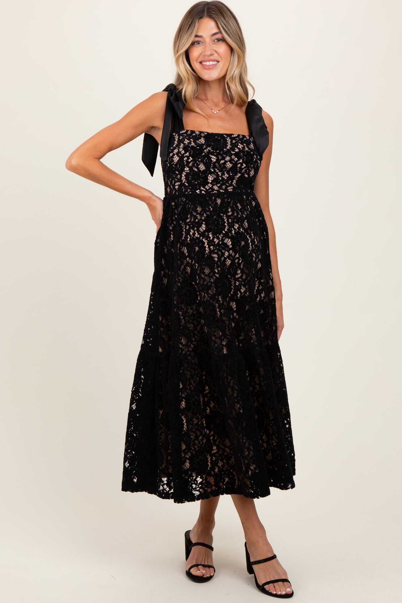 woman wearing a black lace maternity dress with ribbon straps and a flowing skirt showing her baby bump