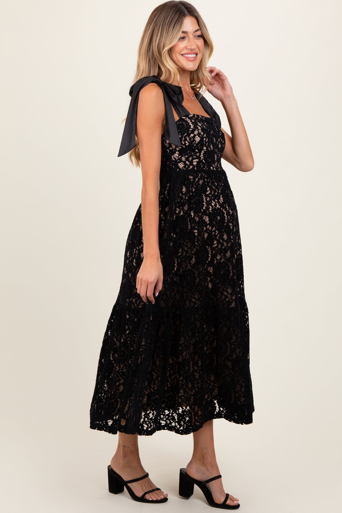 woman wearing a black lace maternity dress with bow tie straps and flowy skirt, showcasing her baby bump