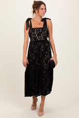 woman wearing a black lace midi dress with bow straps and holding a small black clutch