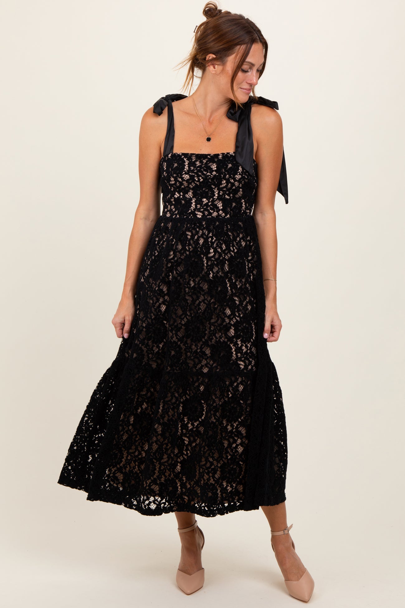 woman wearing a black lace maxi dress with tie straps and a fitted bodice, standing and smiling