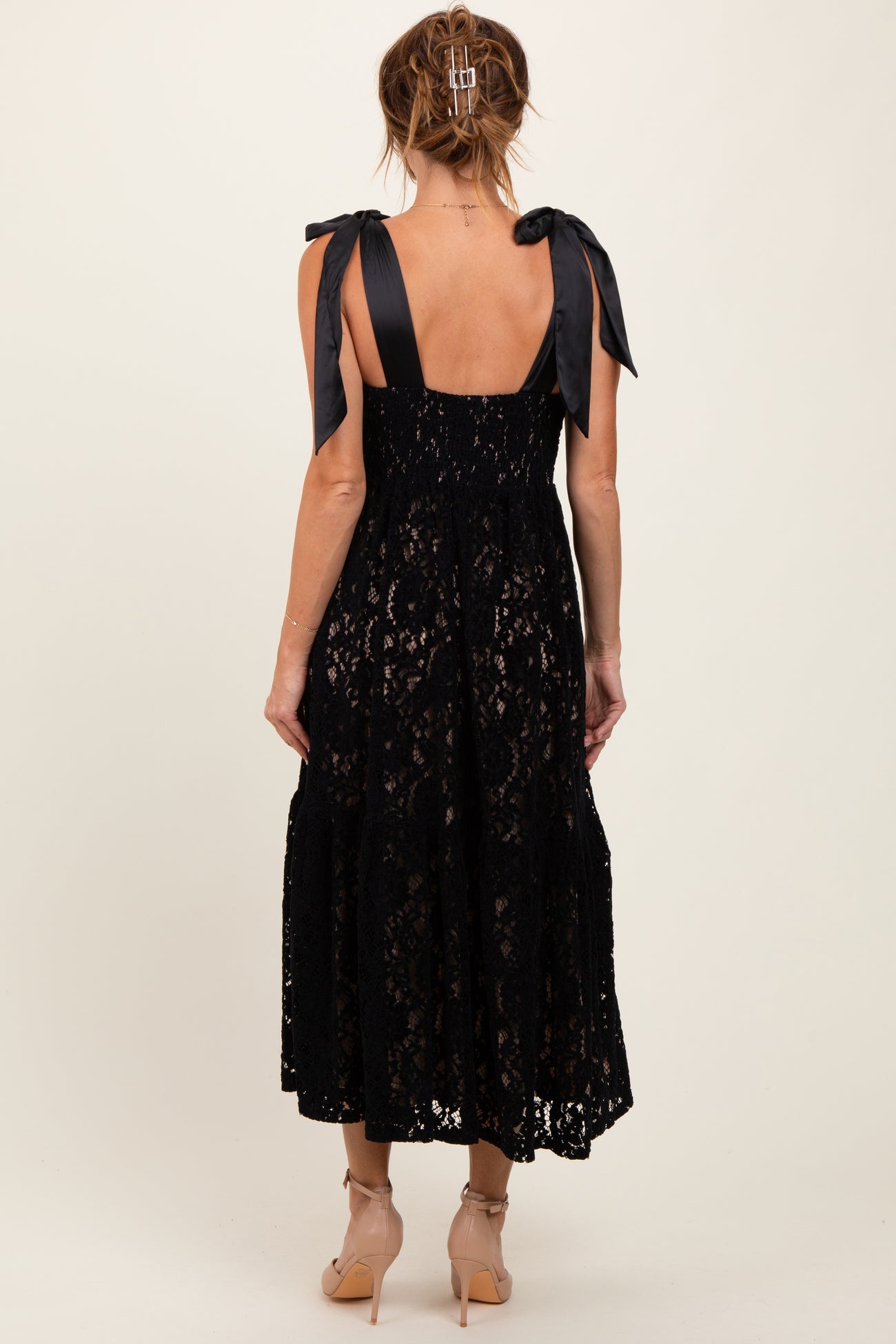 woman wearing a black lace midi dress with ribbon shoulder straps, showing the back view and a flowy skirt