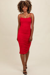 woman wearing a red bodycon midi dress with ruching and embellishments, styled with strappy black heels