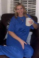 woman wearing a blue loungewear set, sitting on a couch and holding a white mug