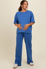 woman wearing a blue maternity top and matching pants, holding her baby bump