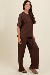 woman wearing a brown ribbed short sleeve top and matching wide-leg pants, standing against a neutral background