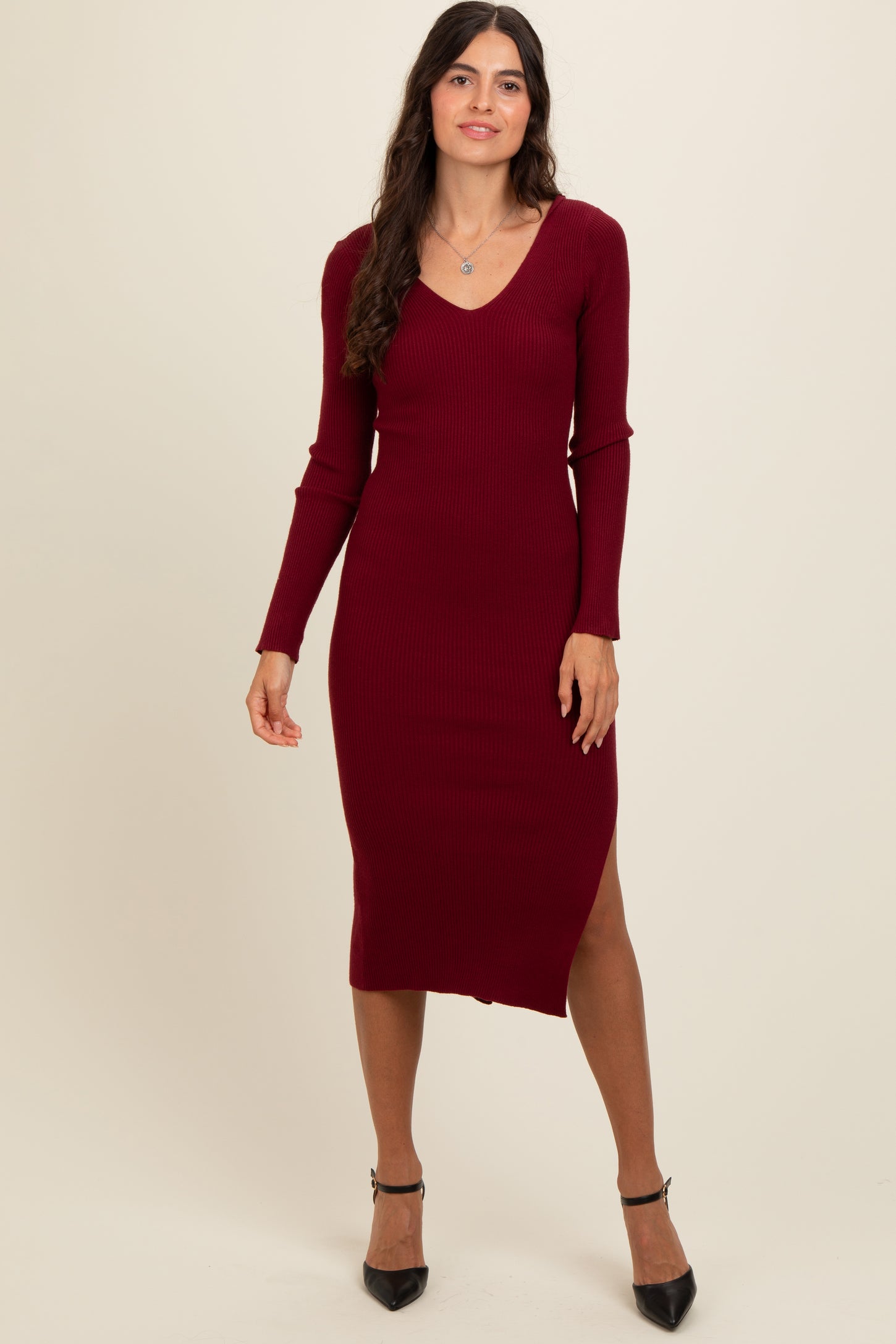 woman wearing a burgundy ribbed midi dress with a v-neck and side slit, paired with black heels