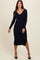 woman wearing a navy ribbed midi dress with long sleeves and a side slit, standing in a relaxed pose
