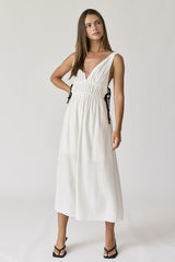 woman wearing a white sleeveless maxi dress with a plunging neckline and tie details at the waist