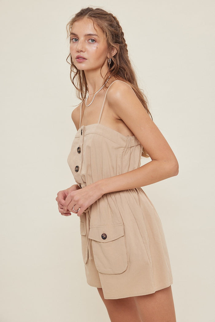 woman wearing a beige button-front romper with adjustable straps and side pockets