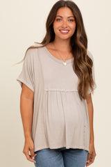 woman wearing a taupe maternity top with a flared hem and short sleeves, showcasing her baby bump