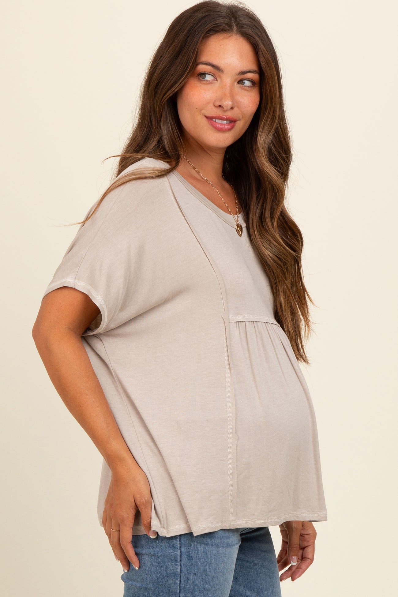 woman wearing a beige short sleeve maternity top with a gathered waist and visible baby bump