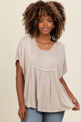 woman wearing a taupe oversized top with short sleeves and a gathered front detail, paired with blue jeans