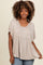 woman wearing a taupe oversized top with short sleeves and a gathered front detail, paired with blue jeans