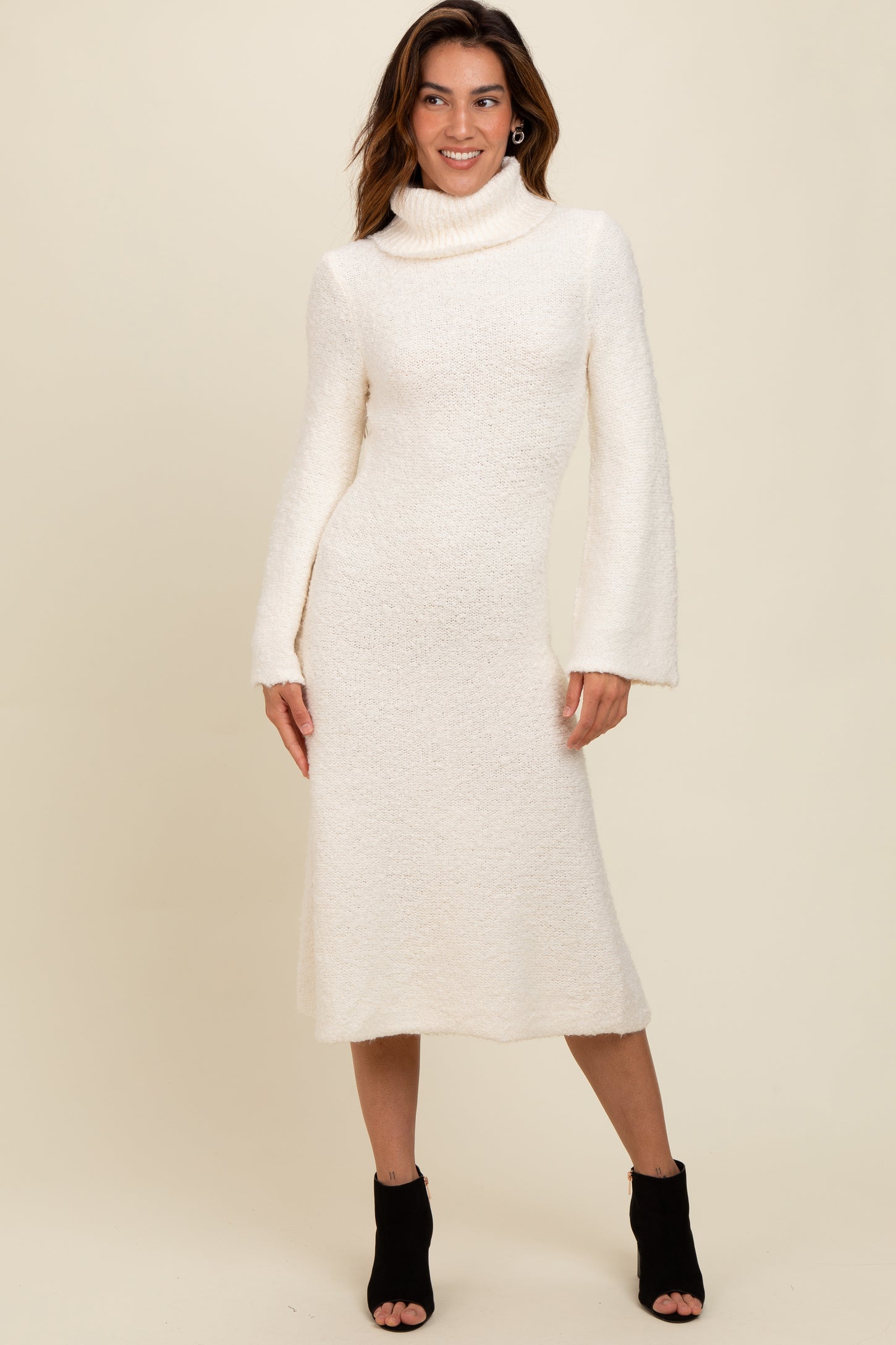 woman wearing a cream-colored long sleeve sweater dress with a cowl neck and bell sleeves, posing against a neutral background