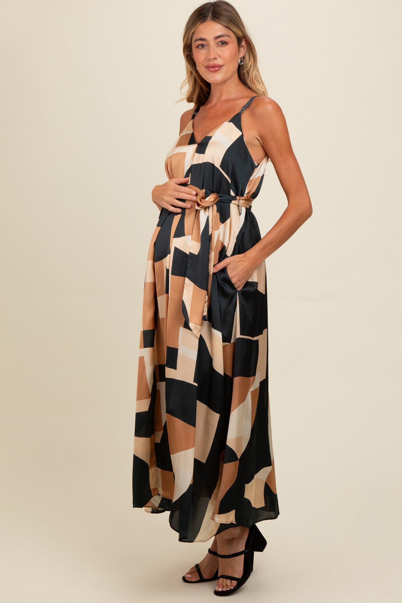 woman wearing a black and beige geometric print maternity maxi dress with pockets and a knotted waist, holding her baby bump