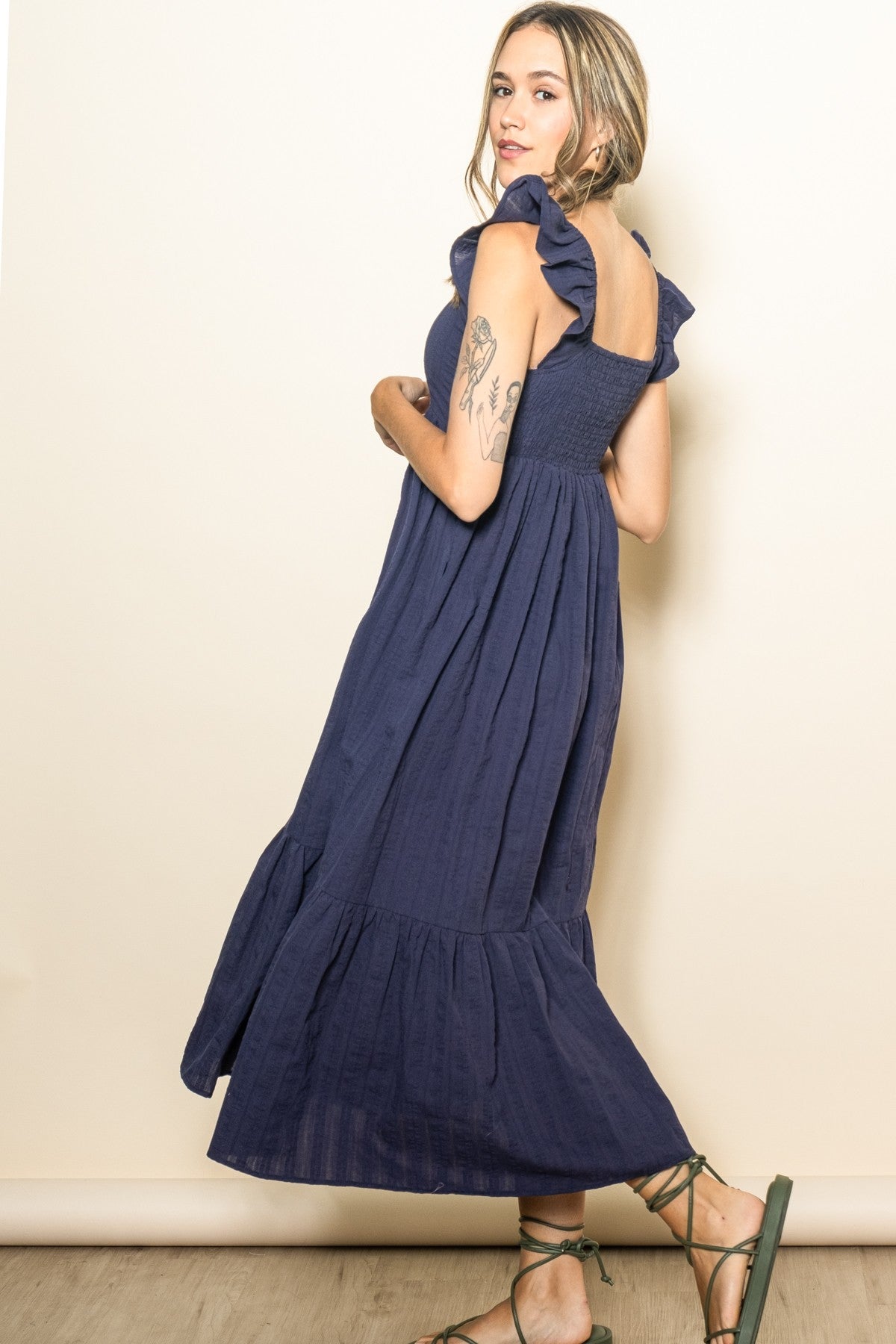 woman wearing a navy blue maxi dress with ruffle sleeves and a tiered skirt, standing sideways against a neutral background