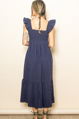 woman wearing a dark blue sleeveless maxi dress with ruffled straps and tiered hem, viewed from the back