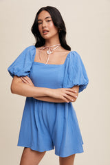 woman wearing a light blue puff sleeve romper with a square neckline and a pink choker necklace