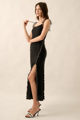 woman wearing a black spaghetti strap dress with ruffle details and a side slit, posing against a neutral background
