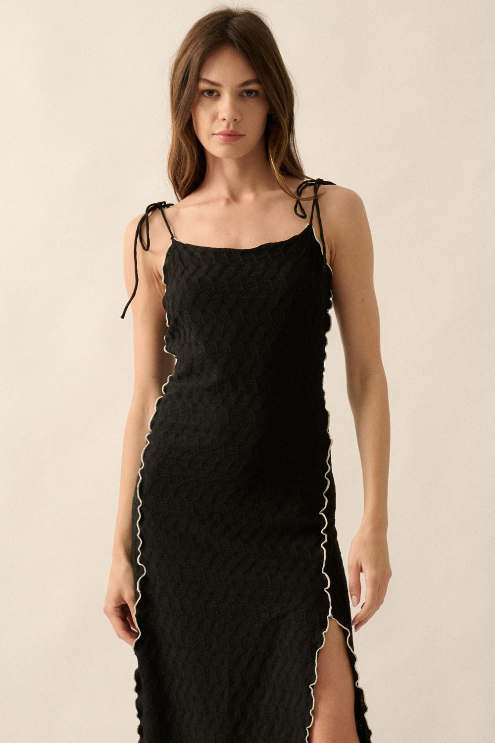 woman wearing a black maxi dress with a textured pattern and white trim detailing, featuring adjustable straps and a side slit