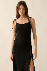 woman wearing a black maxi dress with a textured pattern and white trim detailing, featuring adjustable straps and a side slit