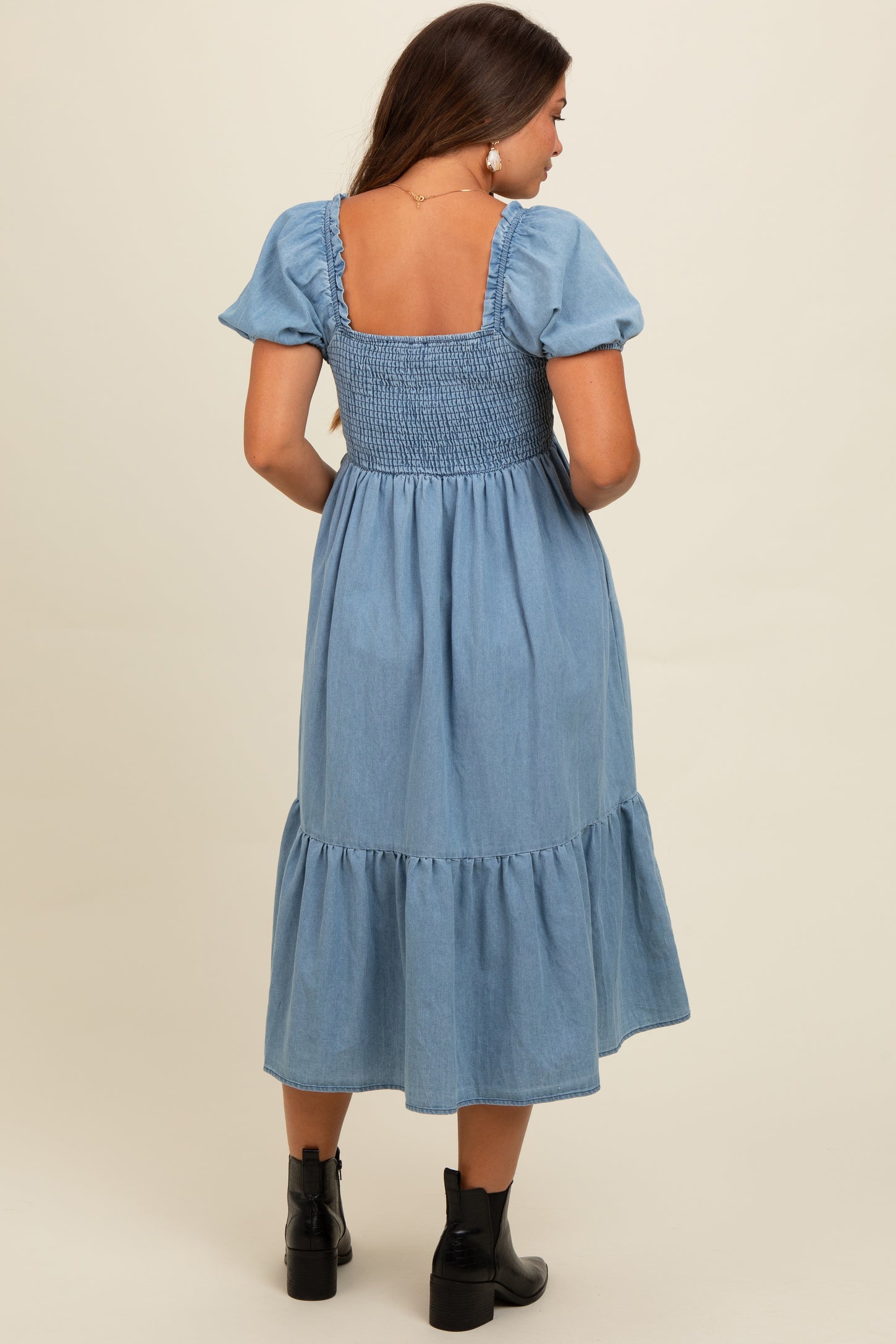 woman wearing a light blue maternity dress with puff sleeves and a smocked bodice, showing a baby bump from the back